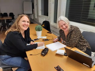 Heidi and Anne sitting at a desk and smiling at the camera